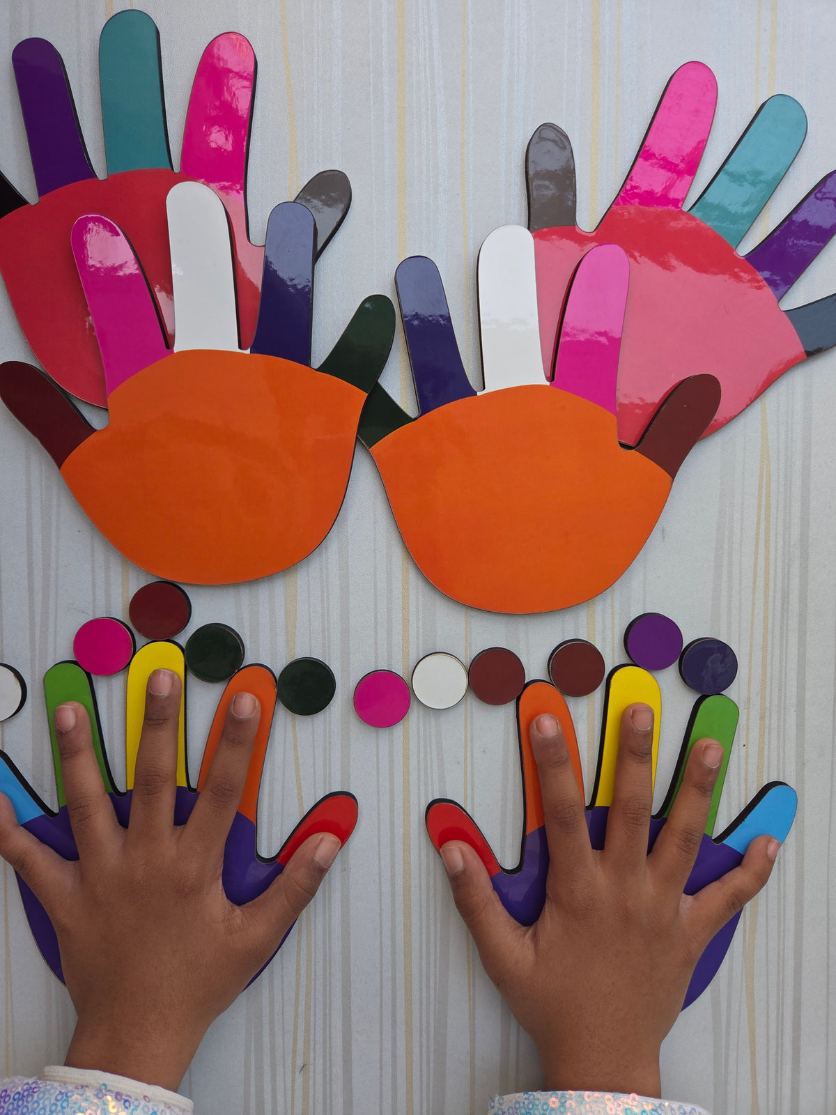 Colorful hand-shaped paper cutouts with children's hands interacting with them on a light background.