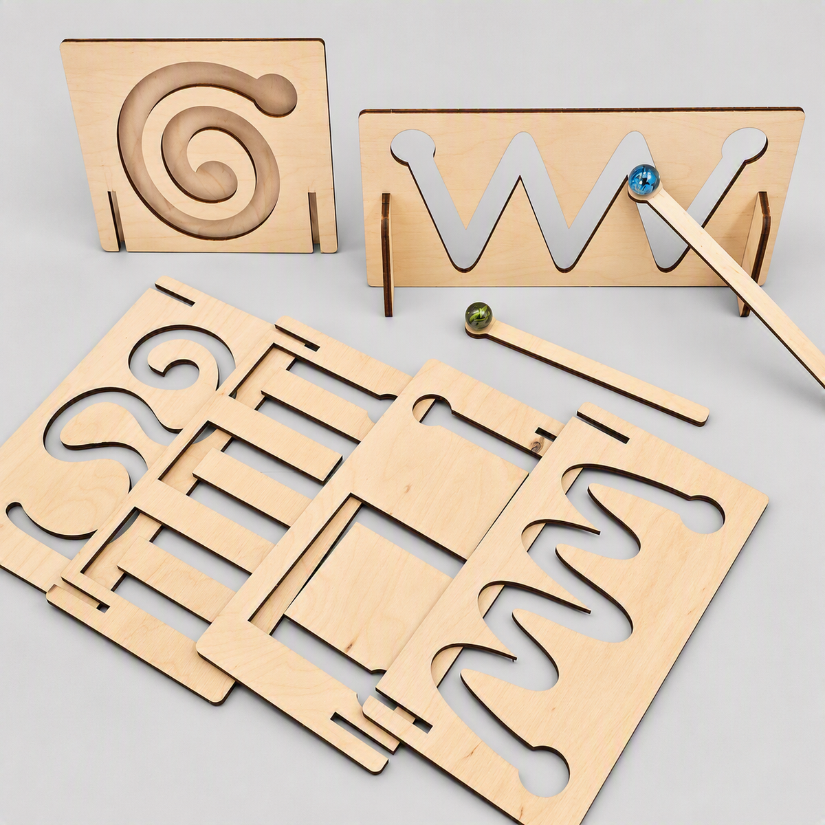 A wooden letter and number learning toy set with laser-cut wooden boards, small wooden dowels, and colorful ball bearings on a light gray background.
